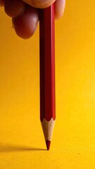 Finger hovers red pencil above sunny yellow background