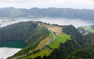 Fototapeta premium Volcanic lake in Sete Cidades, Sao Miguel, Azores. Winding road through green countryside. Caldera landscape with mountains and clouds.