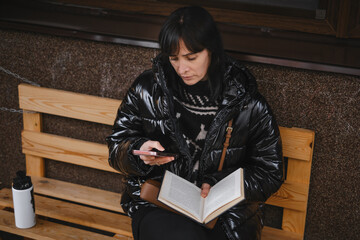 Relaxed reader in warm winter coat enjoys literary moment on rustic bench outside modern cafe...