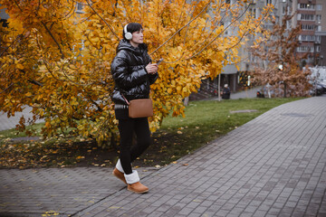 Woman in warm black puffer jacket holds headphones while walking through city park with golden autumn trees, enjoying music outdoors © ninelutsk