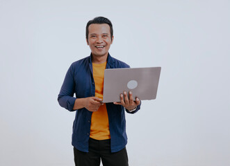 Portrait of young modern asian man standing holding laptop and looking at camera with happy smile, isolated over white background.