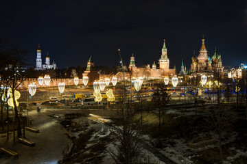 Fototapeta premium Moscow, Russia. View from Zaryadye Park to the Moscow Kremlin, Ivan the Great Bell Tower and St. Basil's Cathedral. Beautiful street lighting and garlands on lanterns. Historical center of Moscow.