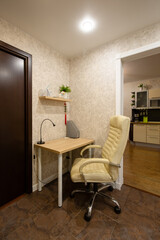 Fototapeta premium Apartment interior. Leather chair near a small desk. Desk lamp on the desk. Shelf on the wall. Compact work area in the hallway of a small apartment. Writing corner. Home mini-office.