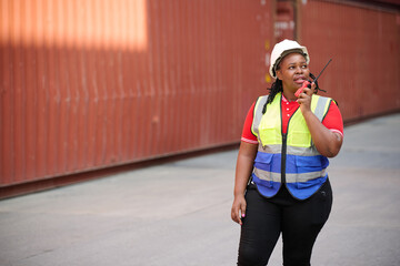 Female worker communicating on a walkie-talkie near a freight container