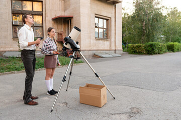 Teacher and student prepare a telescope for astronomical observation outdoors near a building, focusing on proper setup for stargazing and learning