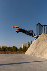 Freerunner pushes off a concrete ramp to start a dynamic backflip under blue sky, demonstrating explosive energy and technique in outdoor urban movement