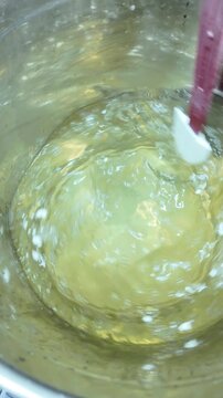Video of a spatula stirring coconut oil and vitamin C powder together in a stainless steel tank.
