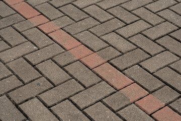 Diagonal red painted line marking a boundary on gray herringbone concrete paving block floor.