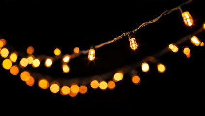 Blurred warm yellow string lights with glowing bulbs on a dark background, festive holiday ambiance