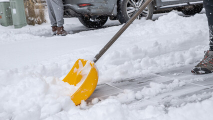Snow cleaning service worker using a yellow shovel to clear snow from a driveway, showcasing winter maintenance and outdoor labor efforts © JuliaDorian
