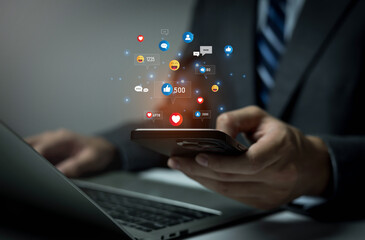Businessman using smartphone and laptop with social media icons, representing online communication, digital marketing, customer engagement, networking, social interaction, modern business technology.