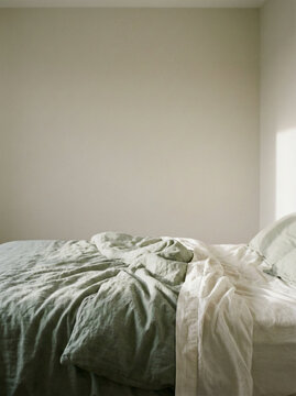 Minimalist bedroom interior with an unmade bed and soft natural sunlight casting gentle shadows on neutral walls