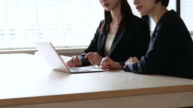 オフィスでパソコンを見て悩むスーツを着た2人の日本人女性