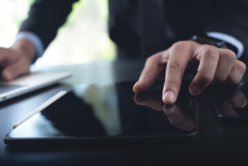 Businessman using digital tablet and  working on laptop computer on table at office. Business man finger touching on tablet screen at desk and suring the internet, close up