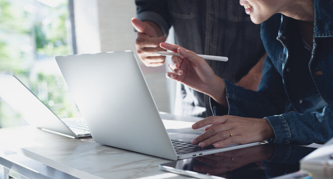 Close up of two asian colleagues working together, have a disussion and using laptop computer at office with financial document on desk