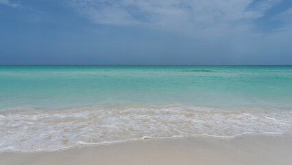 Beautiful minimalistic seascape. The waves of the aquamarine ocean foam and spread over the white sandy beach. Blue sky, clouds. Cuba. Varadero.