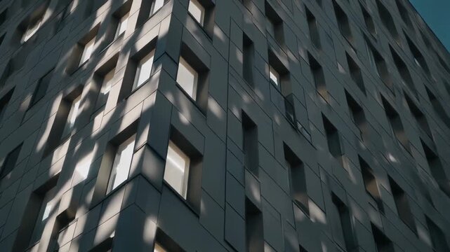 Low angle view of a gray building with rectangular windows, sunlight shining on it