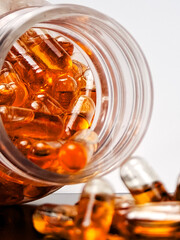 Close up of amber softgel capsules scattered on a gray surface, shot in studio lighting. Modern healthcare and nutrition concept showing vitamin, fish oil, or supplement pills for daily wellness