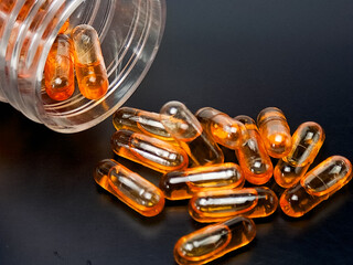 Close up of amber softgel capsules scattered on a gray surface, shot in studio lighting. Modern healthcare and nutrition concept showing vitamin, fish oil, or supplement pills for daily wellness