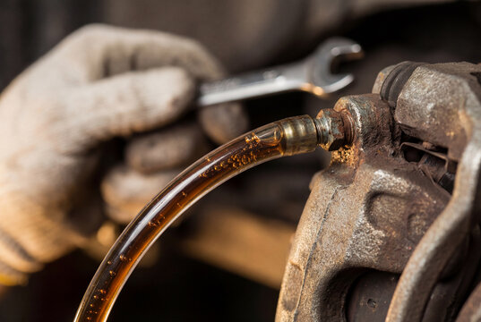 Car brake system bleeding process close-up. Old fluid flowing through tube