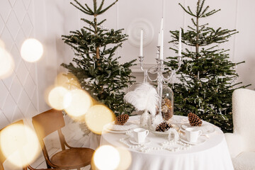 Warm Festive Christmas Table Setting with Pine Cones, Candles, and Feathers in Elegant Scandinavian Interior Decorated with Fir Trees and Fairy Lights