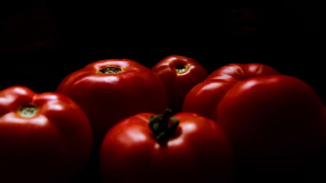 Several ripe, red Beefeater tomatoes are shown in a close-up shot against a dark background. The tomatoes vary slightly in size and shape, some with visible stems or stem scars.