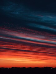 An impressive display of colors in the sky as the sun sets with a dark outline of land beneath.