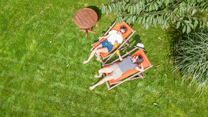 Young girls relax in summer garden in sunbed deckchairs on grass, women friends have fun outdoors...