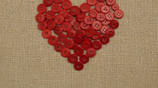 A charming handcrafted heart shape composed of numerous vibrant red buttons, artfully arranged on a rustic beige fabric, symbolizing love, craft, and heartfelt connections