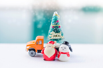 Santa and snowman with Christmas tree on yellow truck over blurred background, Christmas card background idea, festive season concept
