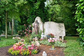 schöner alter Grabstein mit einer großen Jesusfigur und vielen Blumen auf dem Waldfriedhof Memmingen © Blende8