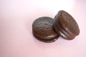 Two Chocolate-Coated Biscuits with Marshmallow Filling on a White Plate, Studio Shot on Pink Background.