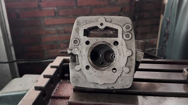 Close up view of an internal combustion engine cylinder head without valve resting on a workshop workbench. Motorcycle Machine Part