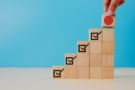 Corporate regulatory and compliance. Goals achievement and business success. Project and goals tracking. Task completion. Managing project timeline. Holding wooden cube with target achievement icon.