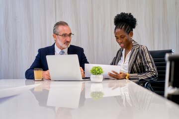 Businessman in formal suit working with his secretary businesswoman in meeting room for summary document with laptop.