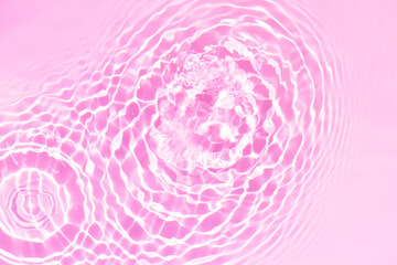 Pink water bubbles on the surface ripples. Defocus blurred transparent pink colored clear calm water surface texture with splash and bubbles. Water waves with shining pattern texture background