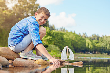 Happy boy, toy and playing with sail ship in lake for outdoor childhood, fun or floating on water....