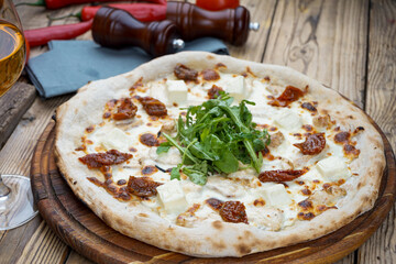 pizza with cheese and sun-dried tomatoes and fresh arugula on a wooden board