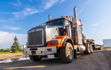 Orange and silver semi truck parked on gravel road in rural landscape