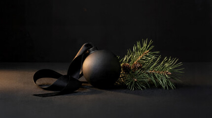 Elegant black Christmas ornament resting on a dark surface with pine branches, creating a minimalist and modern holiday atmosphere
