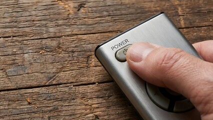 Close-up of Hand Using Remote Control on Wooden Surface.