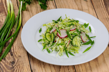 fresh cabbage and radish salad in a white plate on a wooden background with green onions
