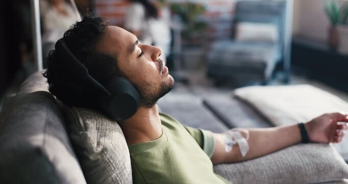Man, headphones and iv drip on couch, relax or listen to music with saline solution for immune system therapy. Person, audio streaming and lounge for wellness benefits, vitamin or mineral infusion