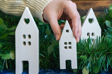 Hand arranging white ceramic houses in festive greenery.