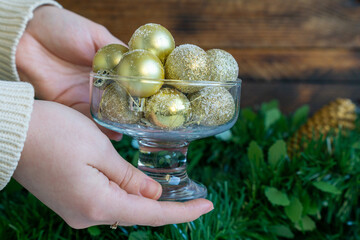 Hands holding a glass bowl filled with gold baubles.