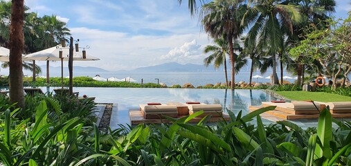 Luxury infinity pool at tropical resort with palm trees and ocean view, comfortable sun loungers on wooden deck, summer vacation and travel background, serene relaxation concept