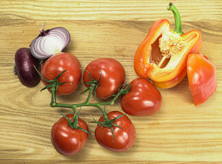 Fresh vegetables, tomatoes on a vine, sliced ​​onions and red peppers on a wooden surface. Healthy eating.