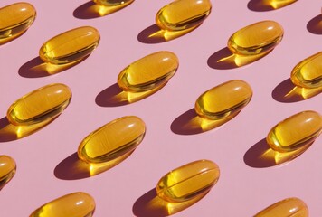 A pattern of yellow fish oil softgels arranged in an orderly fashion on a pastel pink background