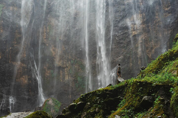 Person admires the grand curtain of water cascading down the rocky face surrounded by greenery