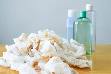 Used makeup remover wipes piled beside micellar water and toner bottles on a wooden surface. Represents daily skincare routine, beauty waste reduction awareness, and cleansing ritual essentials.
